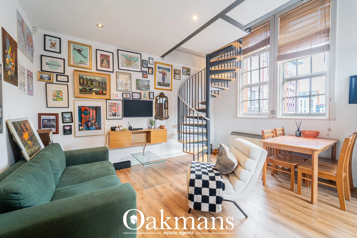 Open-plan living room with green sofa, wooden dining table, spiral staircase, gallery wall art, large windows overlookin