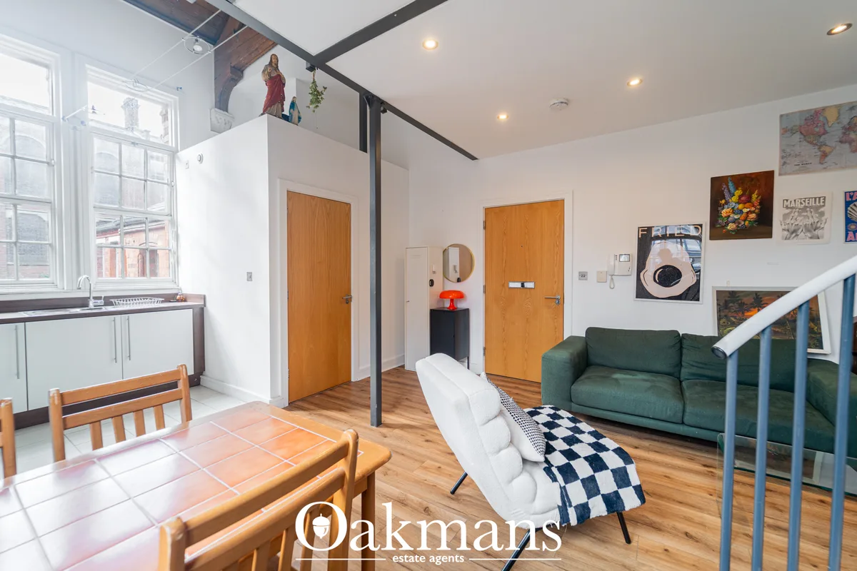Open-plan hallway with wooden doors, white walls, hardwood flooring, green sofa, white bench, kitchen area and staircase