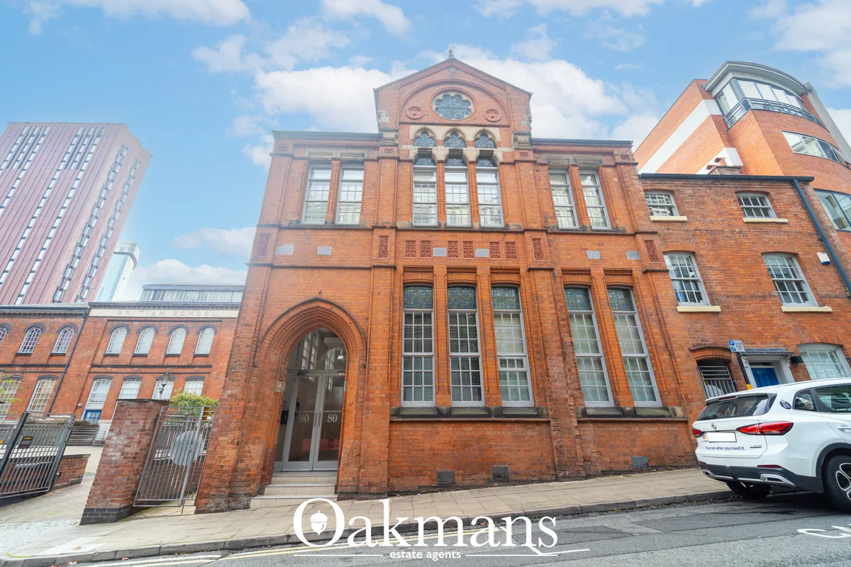 Red brick Victorian building with arched entrance, large windows, circular window detail, and ornamental stonework under