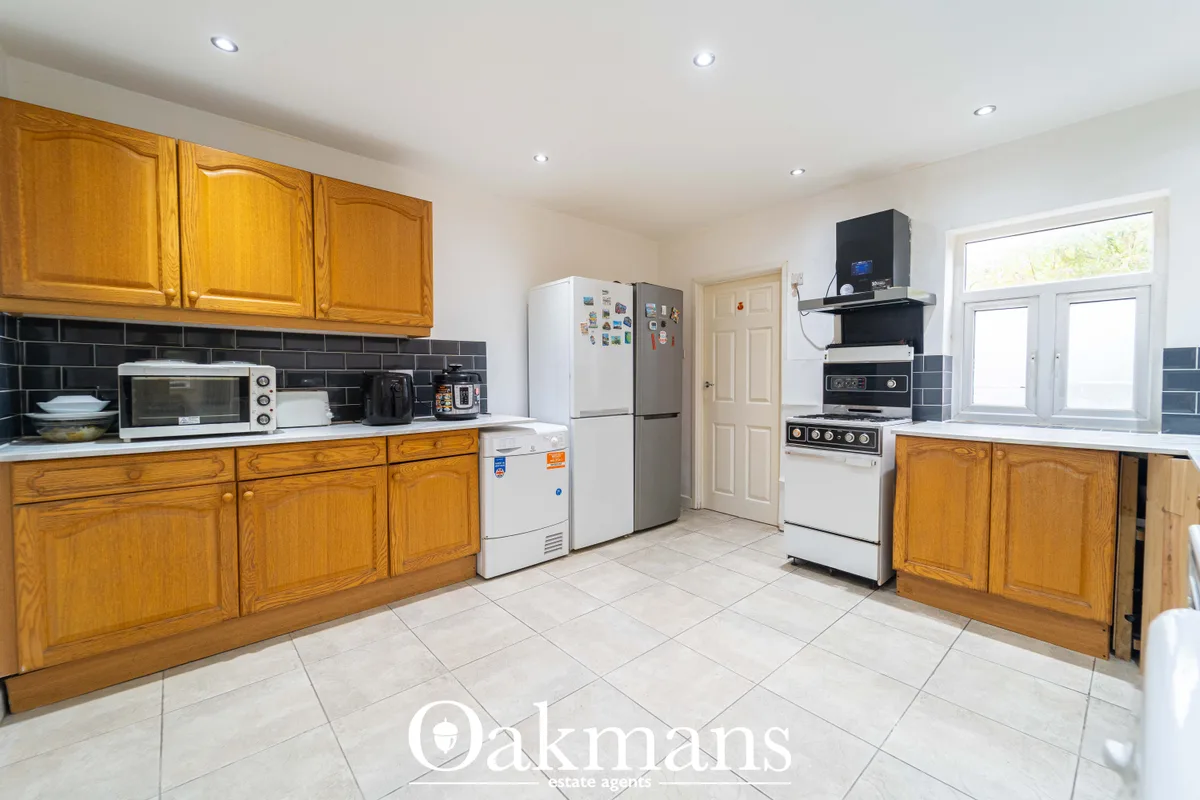 Spacious kitchen with wooden cabinetry, black subway tile splashback, white appliances, tiled flooring and patio doors