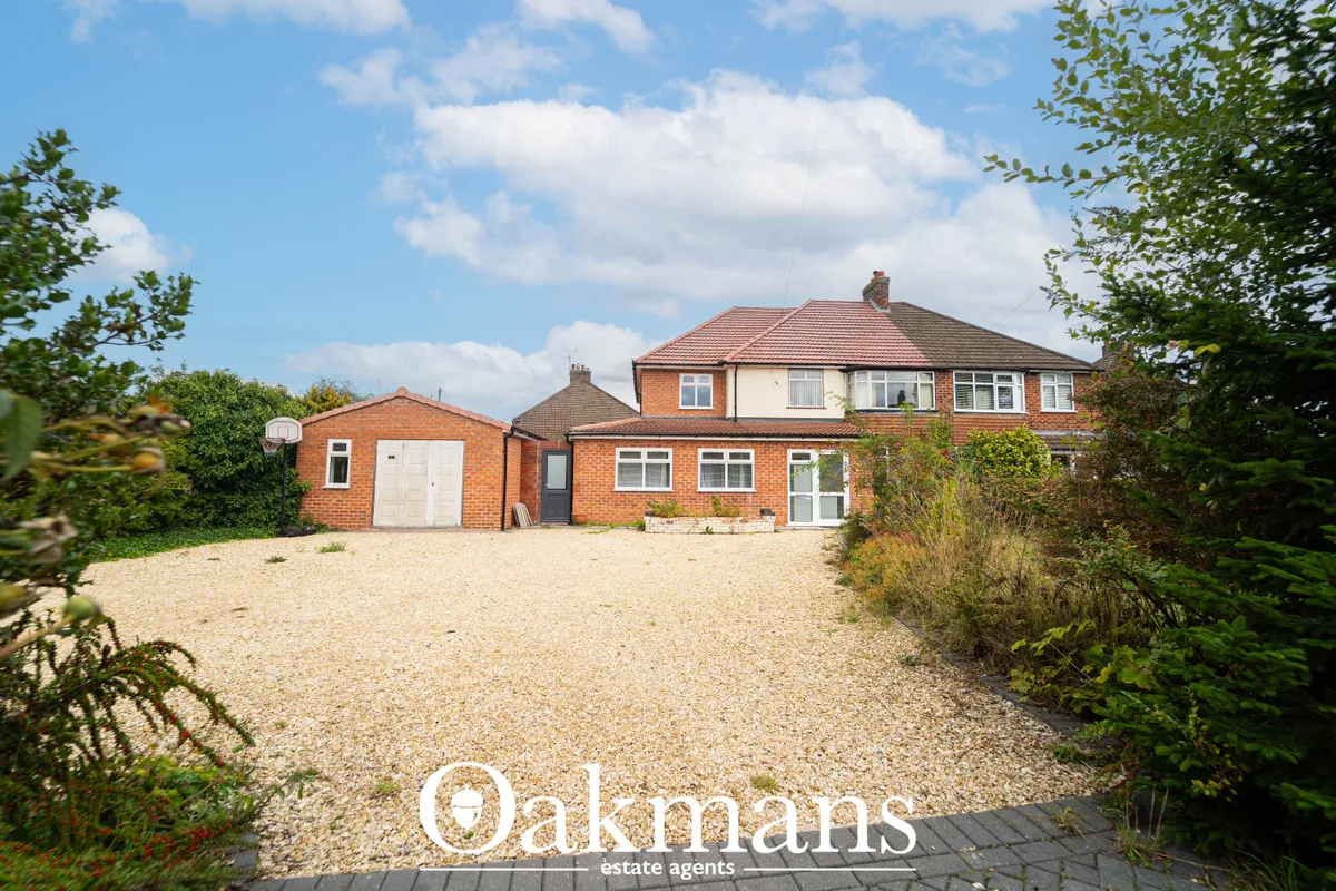 Red brick semi-detached house with driveway, garage, hedged gardens and clear blue sky