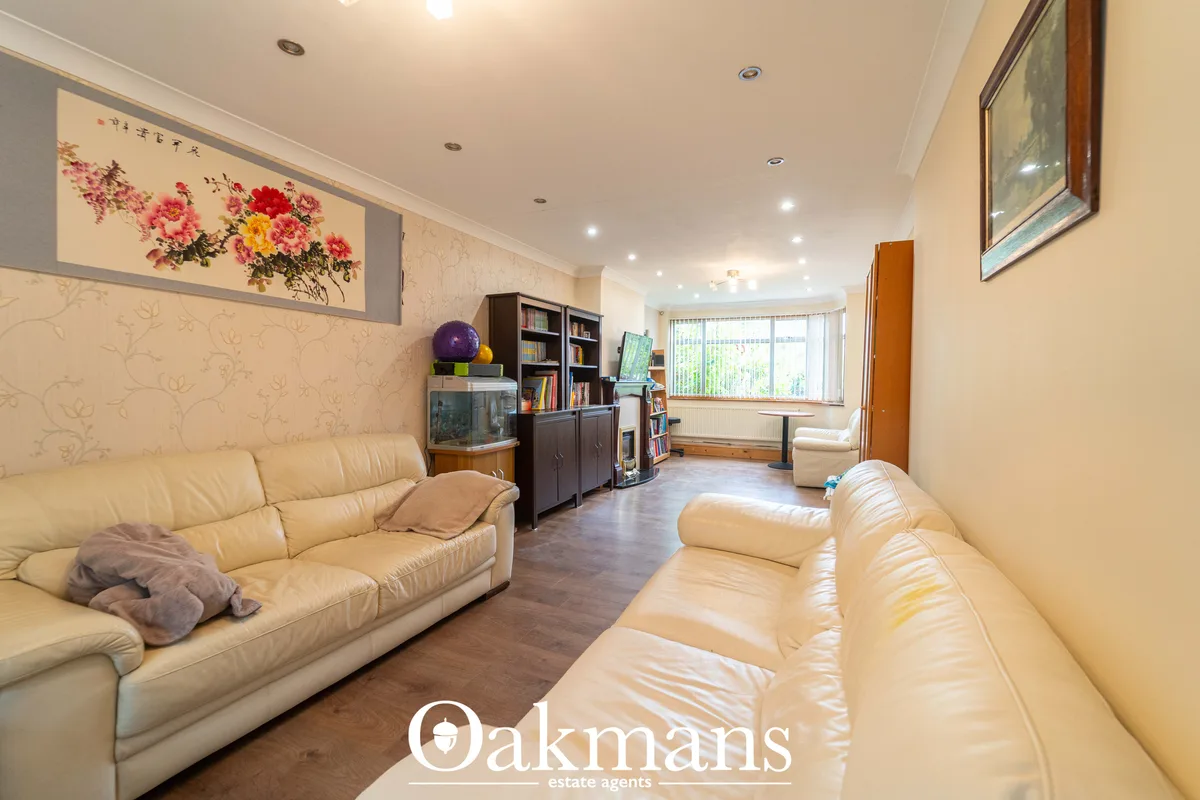 Spacious living room with two cream leather sofas, dark wood storage units, bookshelves, framed artwork, wooden flooring