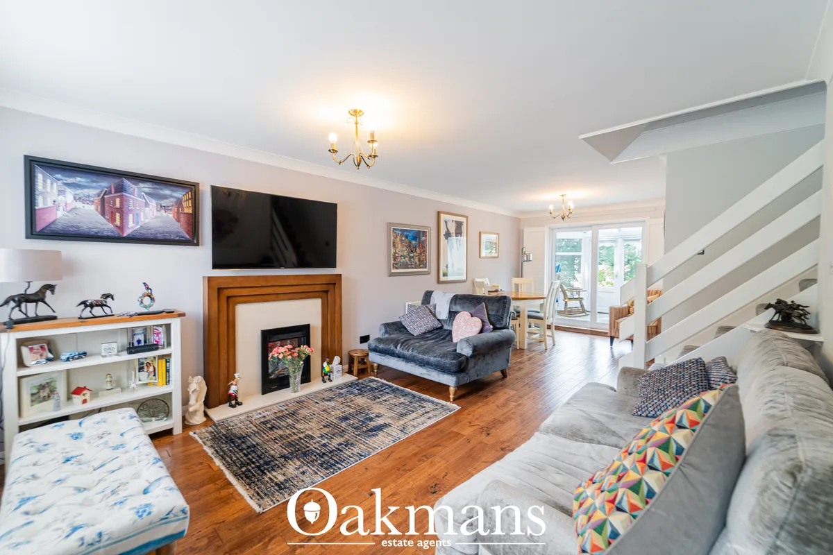 Spacious open-plan living room with wooden flooring, fireplace with wood surround, two sofas, wall-mounted TVs, staircas