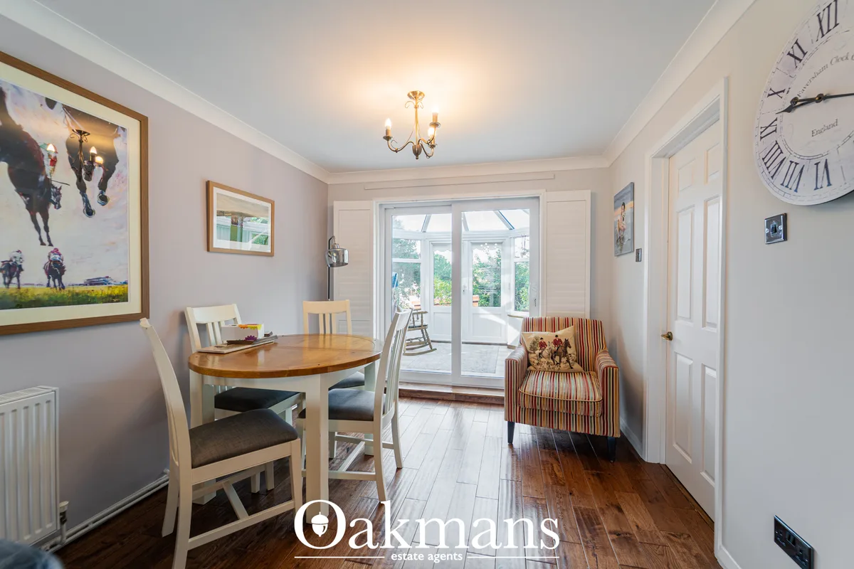 Light-filled dining room with round wooden table, cream chairs, striped armchair, French doors to conservatory, wall art