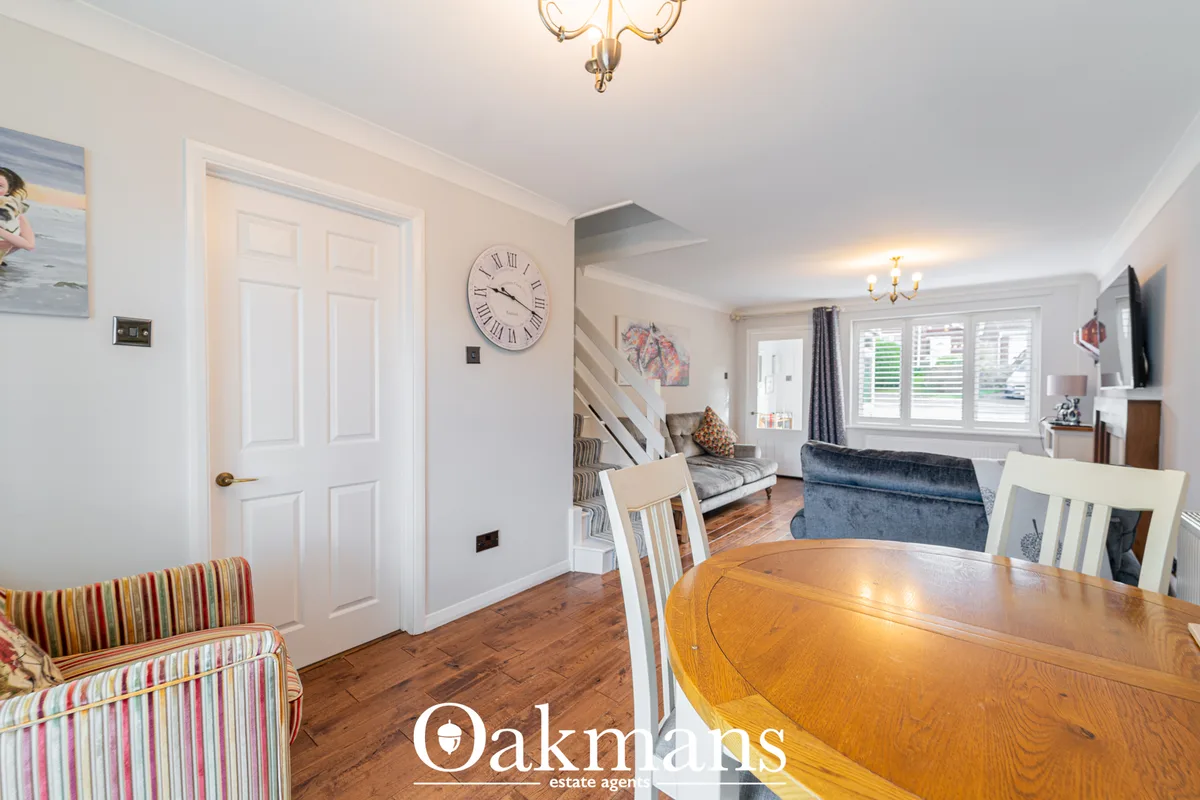 Open-plan dining and living area with wooden dining table, white chairs, striped armchair, and view through to lounge wi