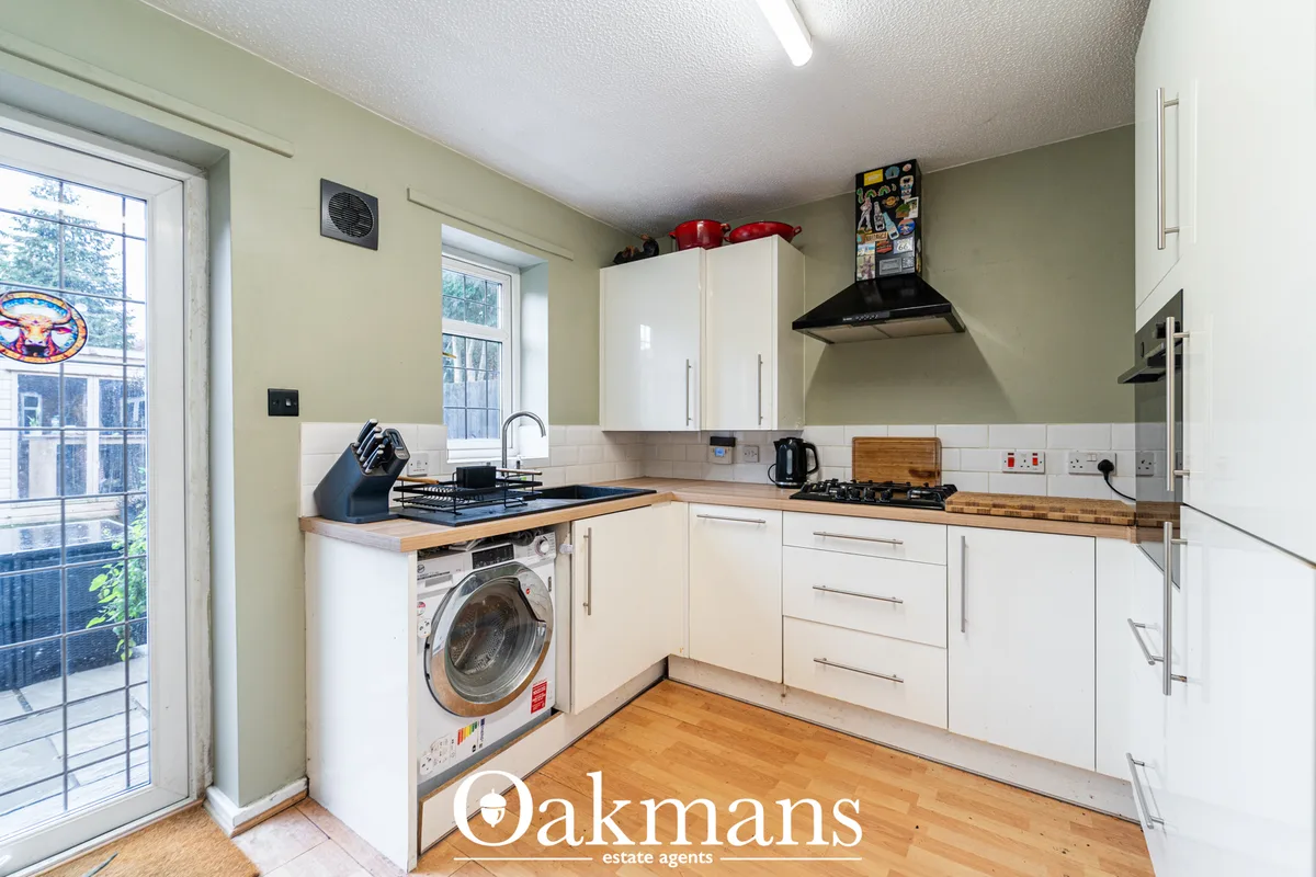 Modern fitted kitchen with white units, wooden worktops, gas hob, black range hood, washing machine and patio doors to g