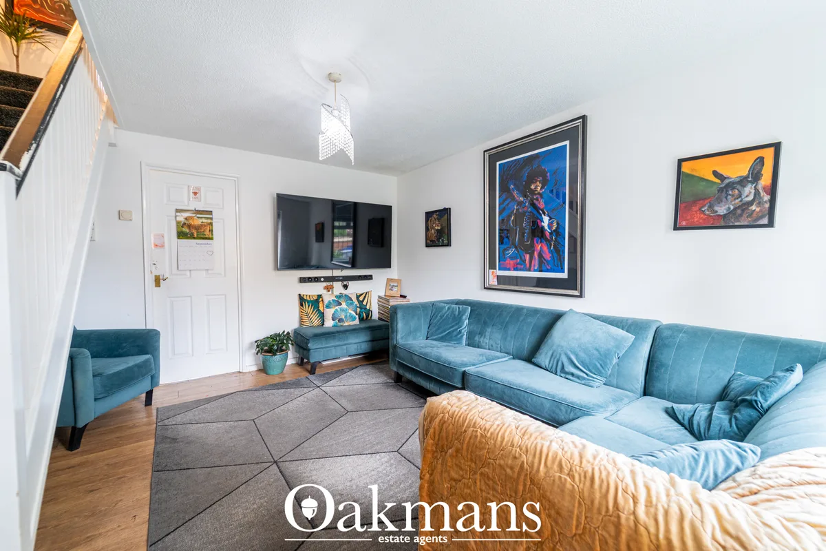 Spacious living room with blue velvet corner sofa, wooden flooring, geometric rug, wall-mounted TV, framed artwork, pend