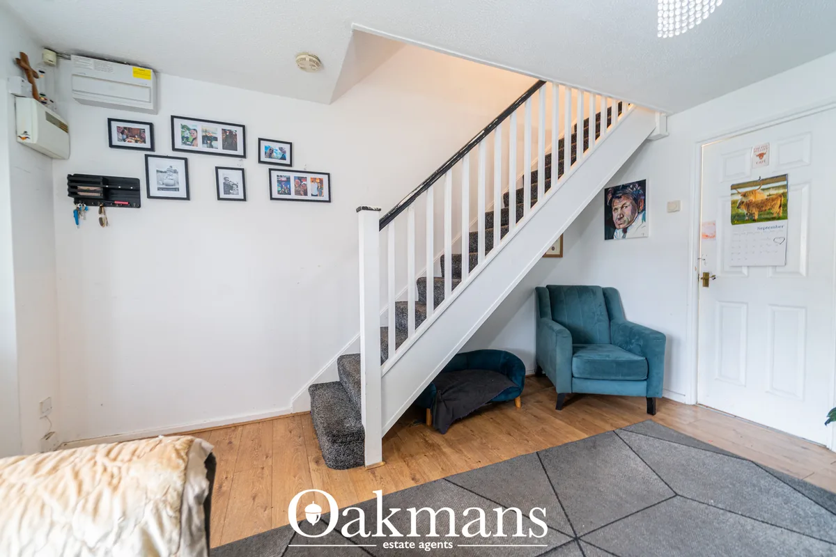 Modern hallway with wooden flooring, white staircase with grey runner, blue armchair under stairs, and framed photograph