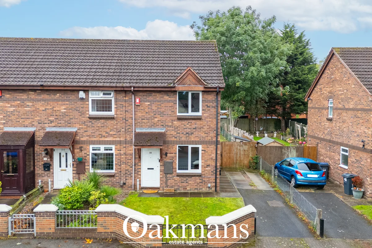 Semi-detached red brick residential properties with dark tile roofs, front gardens, driveways and blue car parked on str
