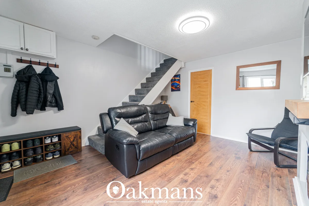 Open-plan living room with black leather reclining sofa, wooden shelving unit, staircase to upper level, wooden flooring