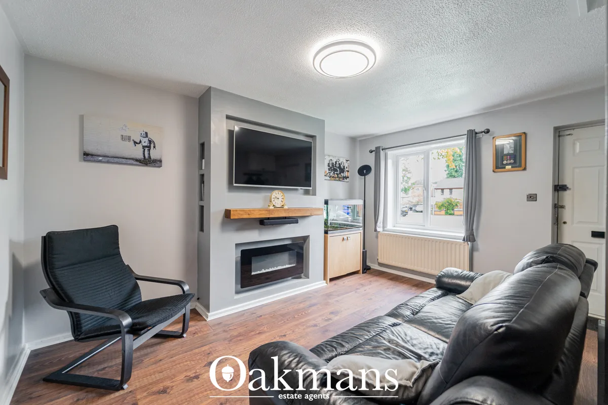Modern living room with black leather sofa, curved armchair, wall-mounted TV above electric fireplace, wooden shelving a