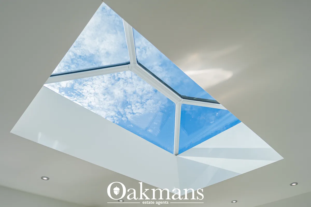 Modern glass conservatory with geometric roof panels, white frame and blue sky visible through glazing
