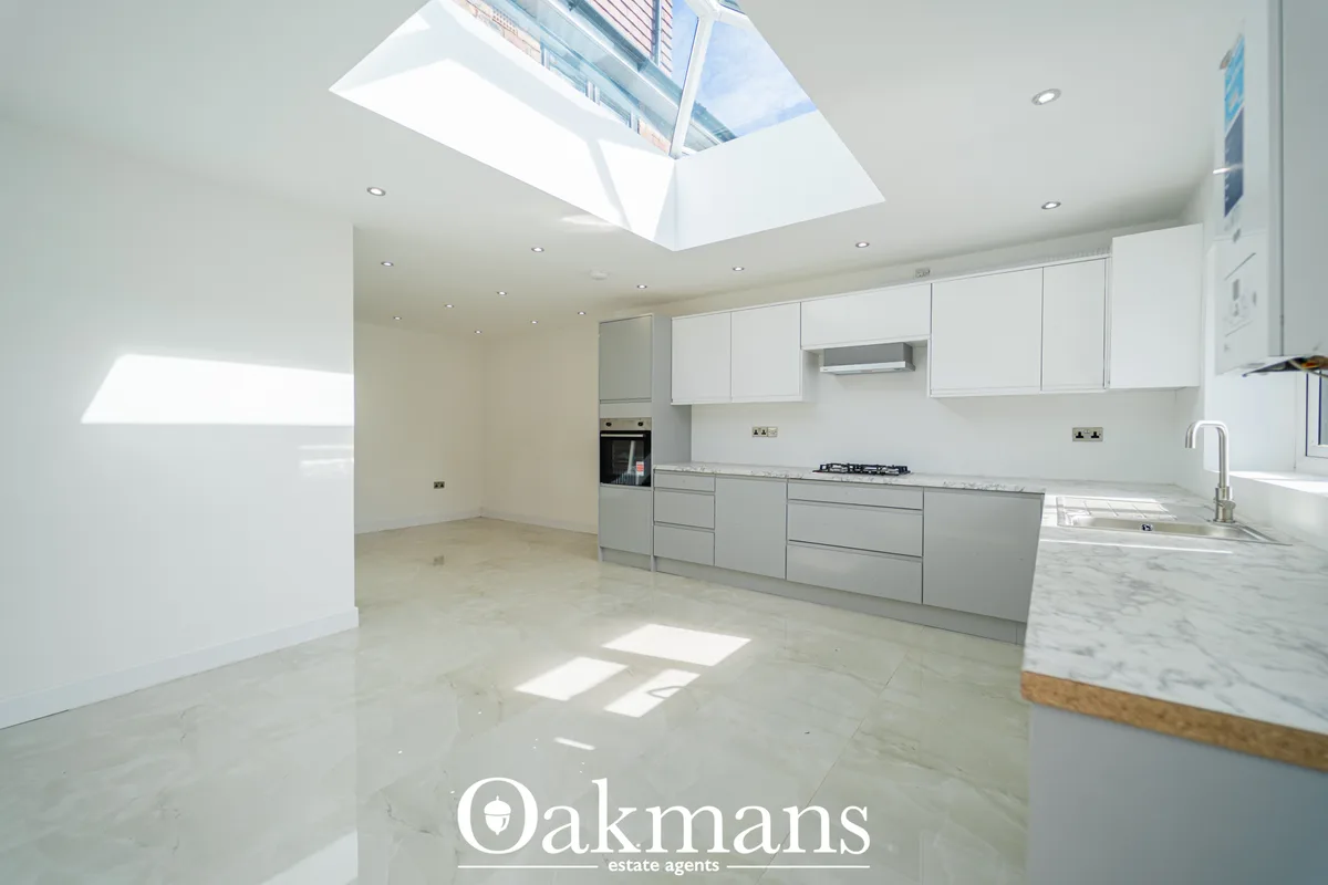 Modern kitchen with white units, marble worktops, integrated appliances, skylight and breakfast bar with wooden trim
