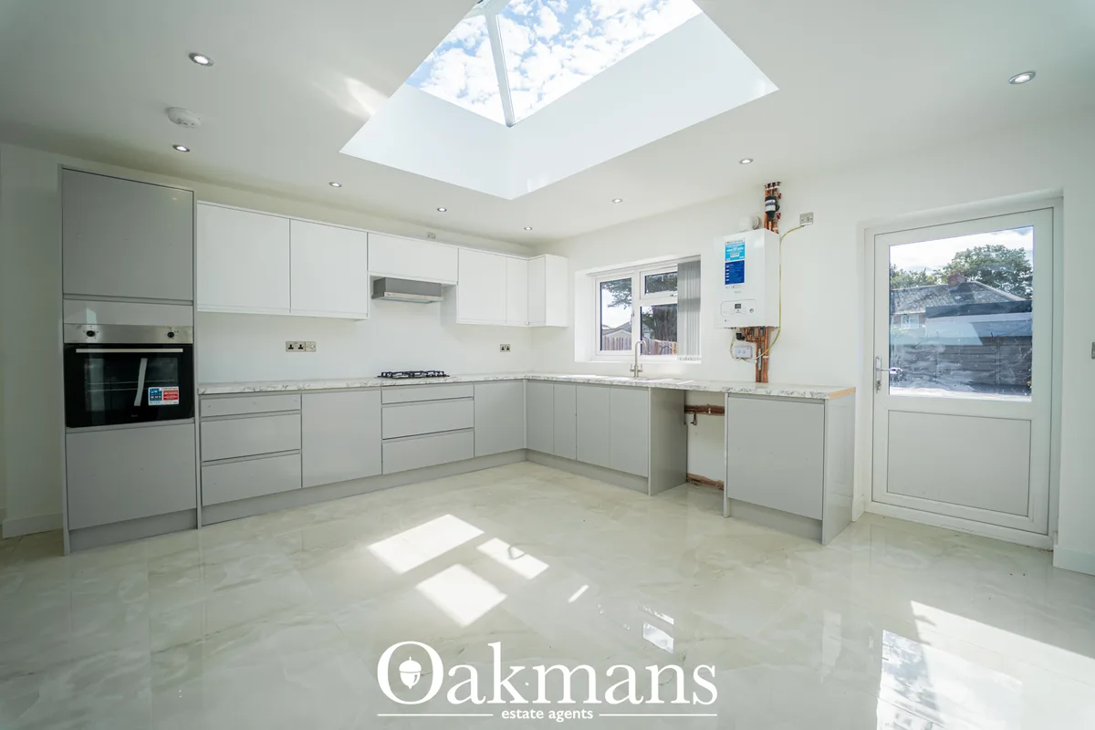 Modern fitted kitchen with white and grey cabinetry, granite worktops, integrated appliances, skylight, and bi-fold door