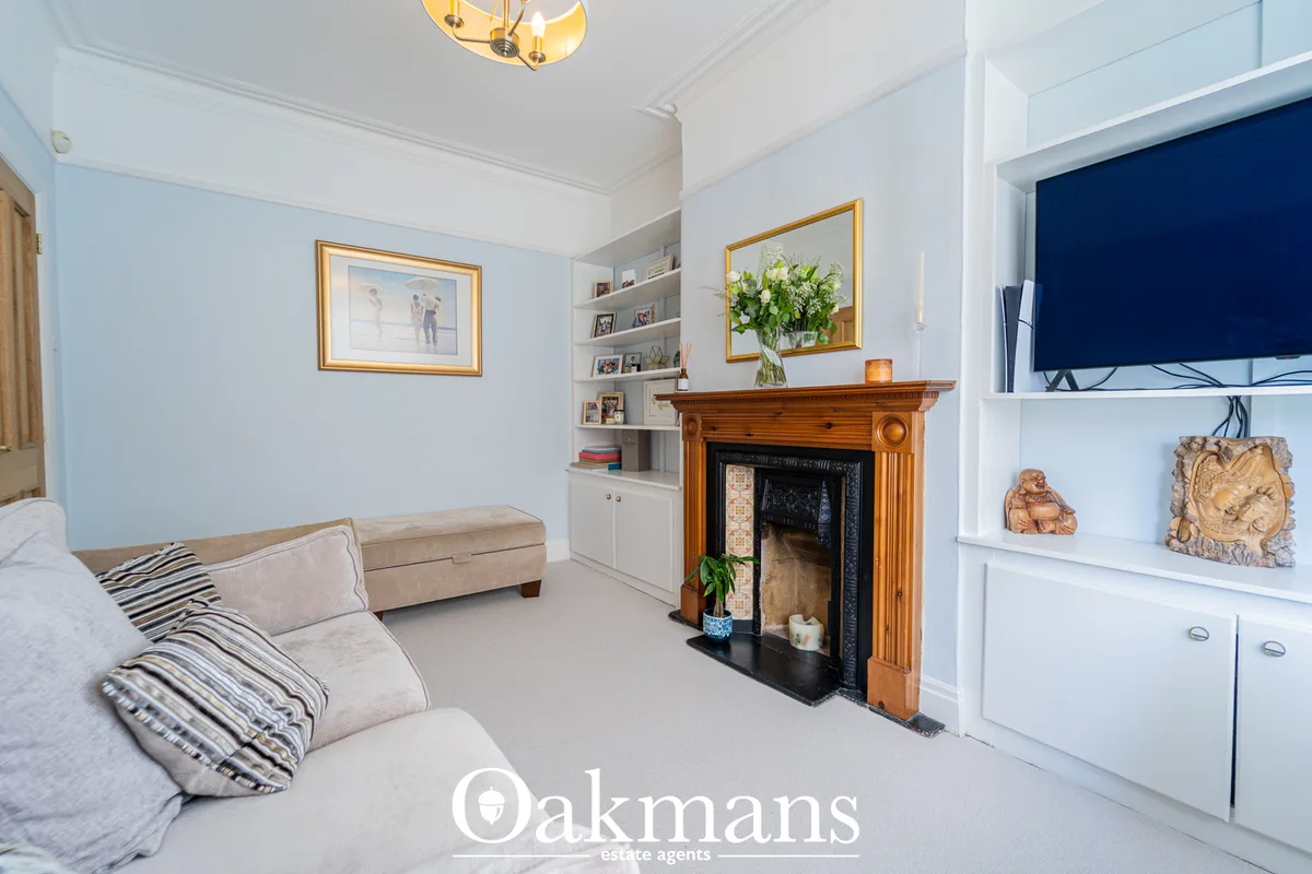Bright living room with beige sofa, wooden fireplace with black surround, white built-in shelving, framed artwork, TV, p