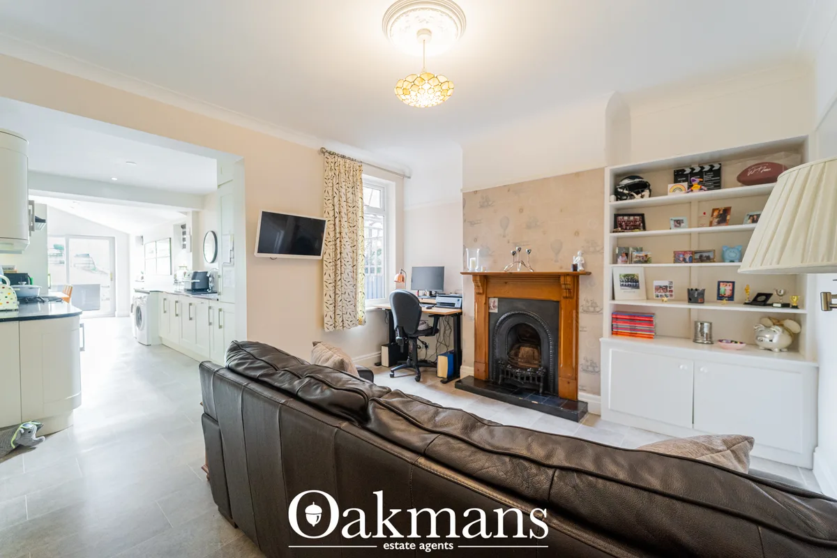 Spacious living room with brown leather sofa, fireplace with wooden surround, built-in shelving, desk area, and open pla