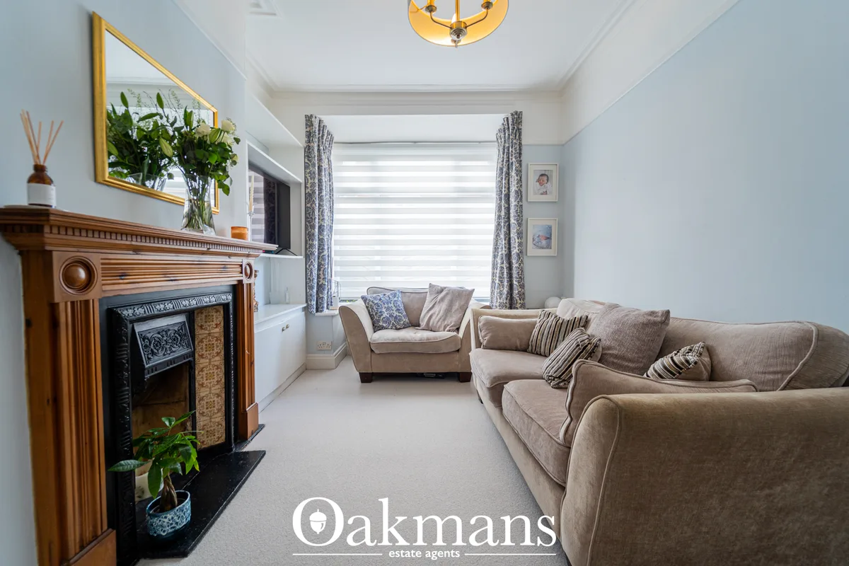 Bright living room with beige upholstered sofas, ornate wooden fireplace with decorative insert, large bay window with p