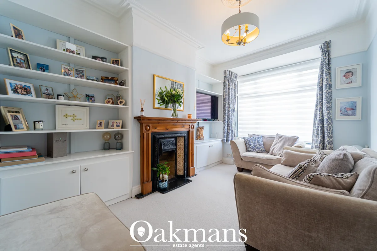 Bright living room with cream sofas, fireplace, built-in shelving, bay window with blue patterned curtains and pendant l