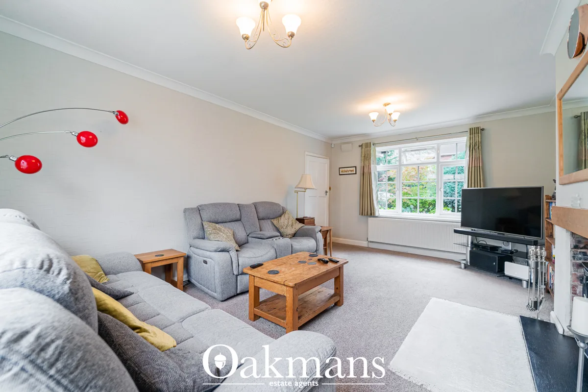 Spacious living room with grey upholstered sofa and recliner, wooden coffee table, TV on stand, large bay window with ga