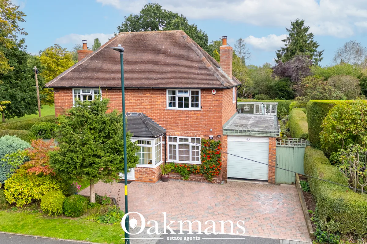 Red brick detached house with pitched roof, white windows, integrated garage, brick driveway and mature landscaped garde