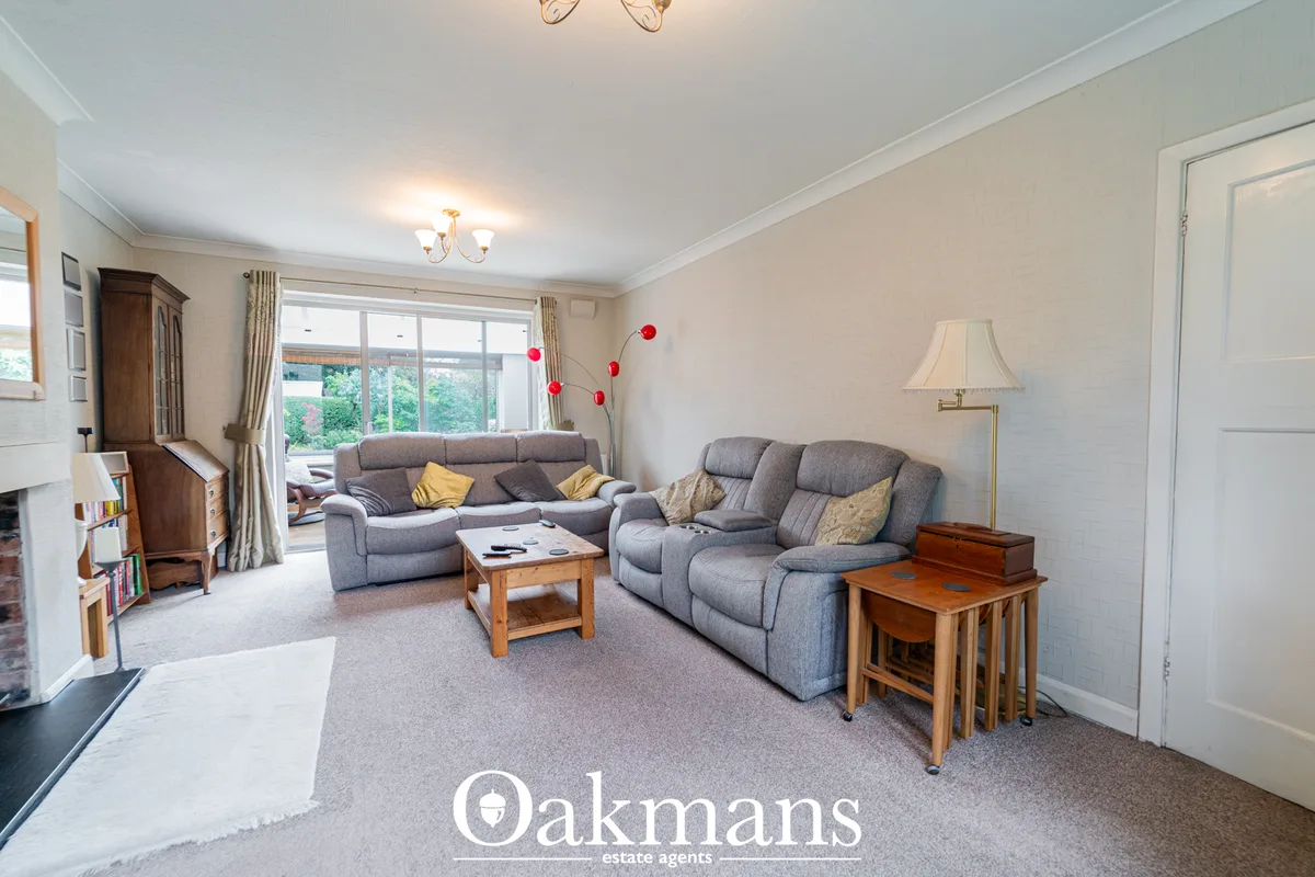 Spacious living room with grey reclining sofas, wooden coffee table, wall-mounted lamp, large bay windows with garden vi