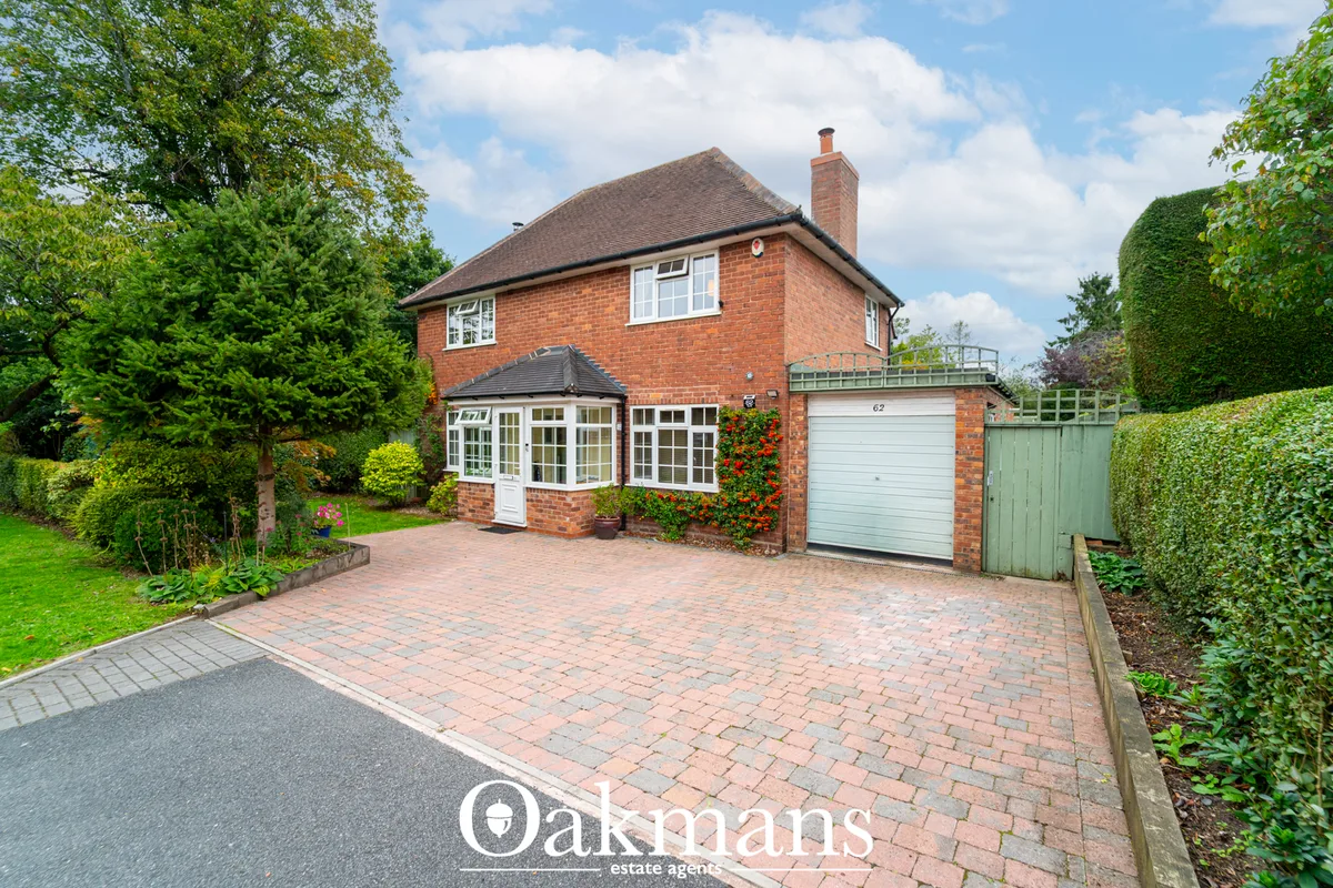 Red brick detached house with white-framed conservatory, pitched roof, brick driveway, and mature hedged garden boundari