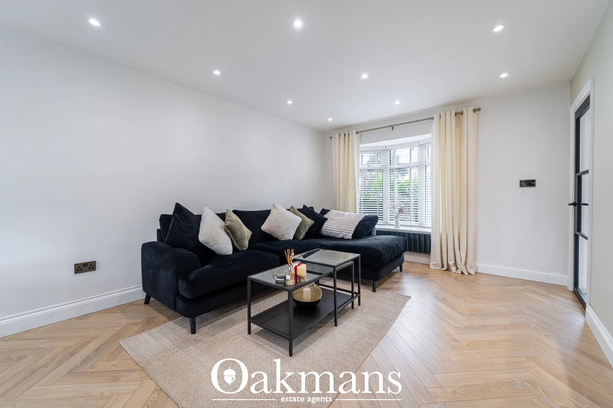 Modern living room with navy corner sofa, cream cushions, glass coffee table on beige rug, wooden herringbone flooring, 