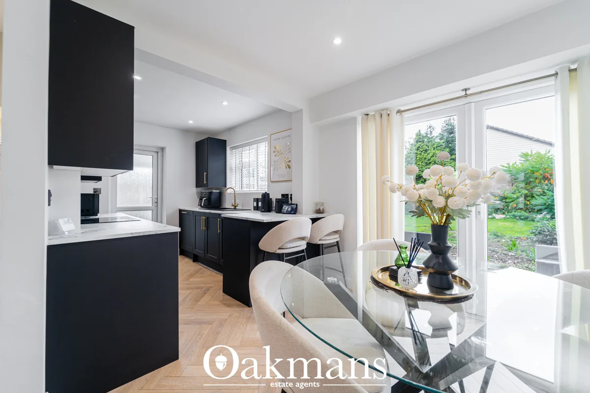 Modern open-plan kitchen with black cabinetry, white worktops, island seating, and patio doors overlooking garden
