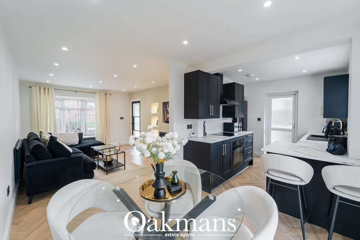 Open-plan living area with black sofa, white dining table, black kitchen units, recessed lighting and wooden flooring th
