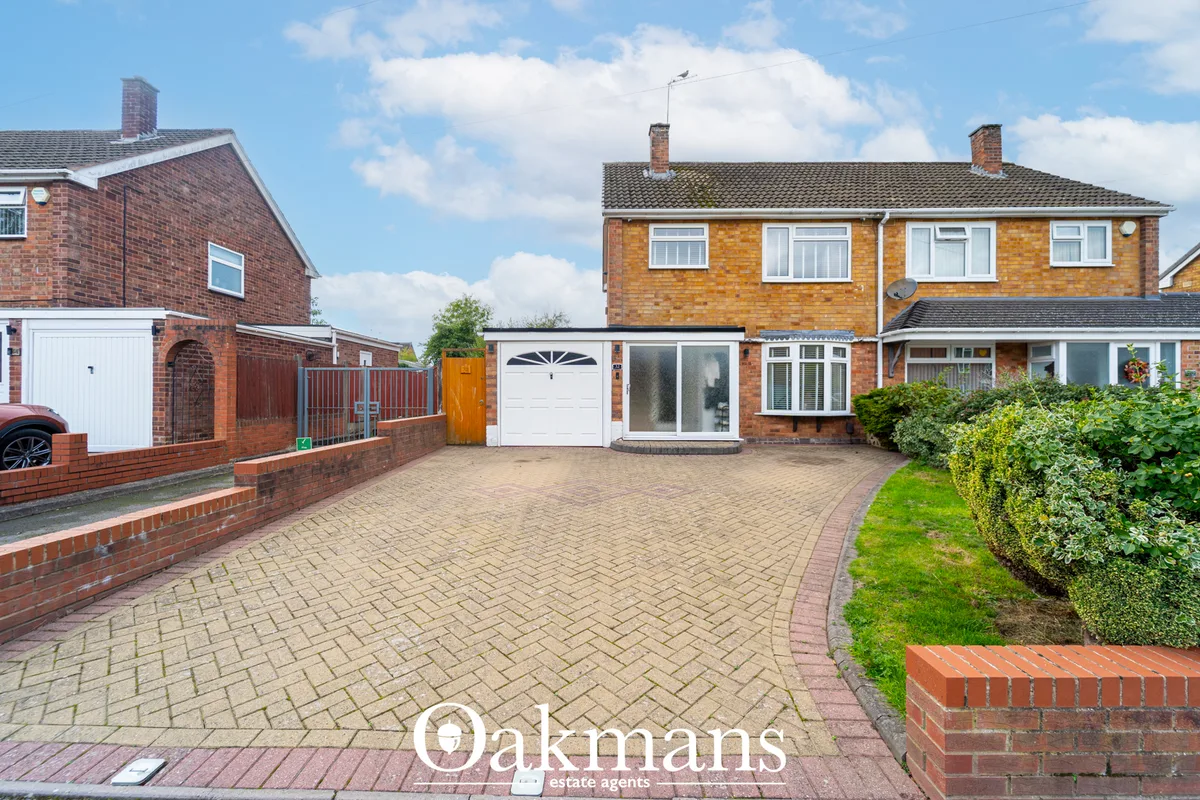 Brick-built semi-detached house with white garage door, driveway, manicured garden and neighboring properties