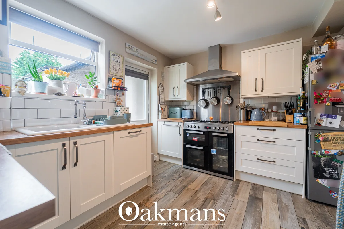 Modern fitted kitchen with cream units, wooden worktops, black double oven, stainless steel range hood, white subway til