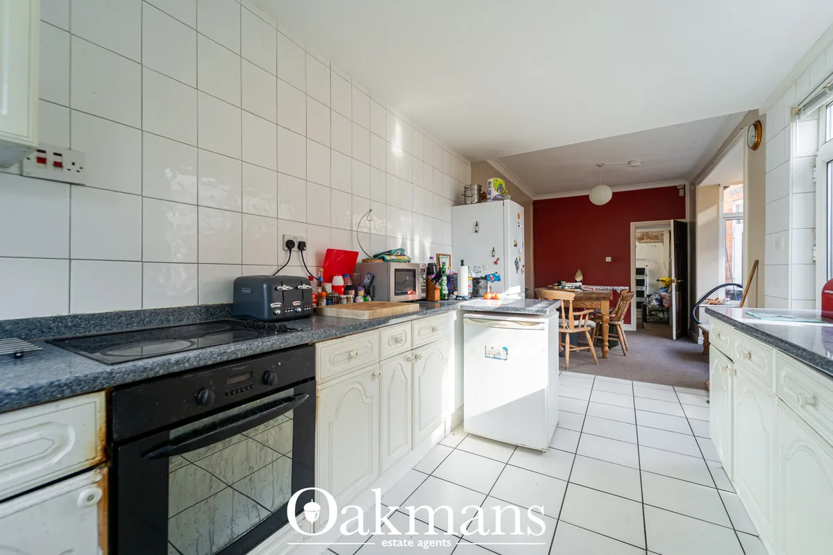 Open-plan kitchen with cream cabinetry, granite worktops, black oven, white appliances and white tile flooring, opening 