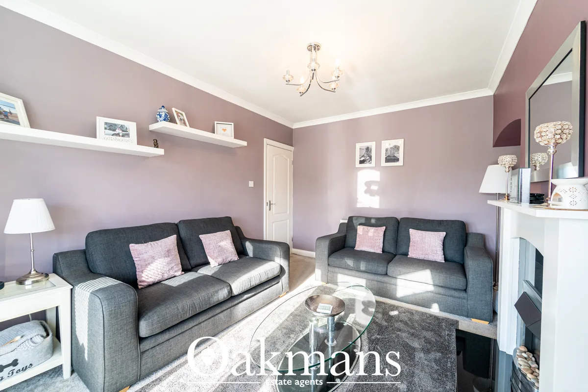 Elegant living room with mauve walls, two grey sofas, glass coffee table, fireplace, white shelving, chandelier and natu