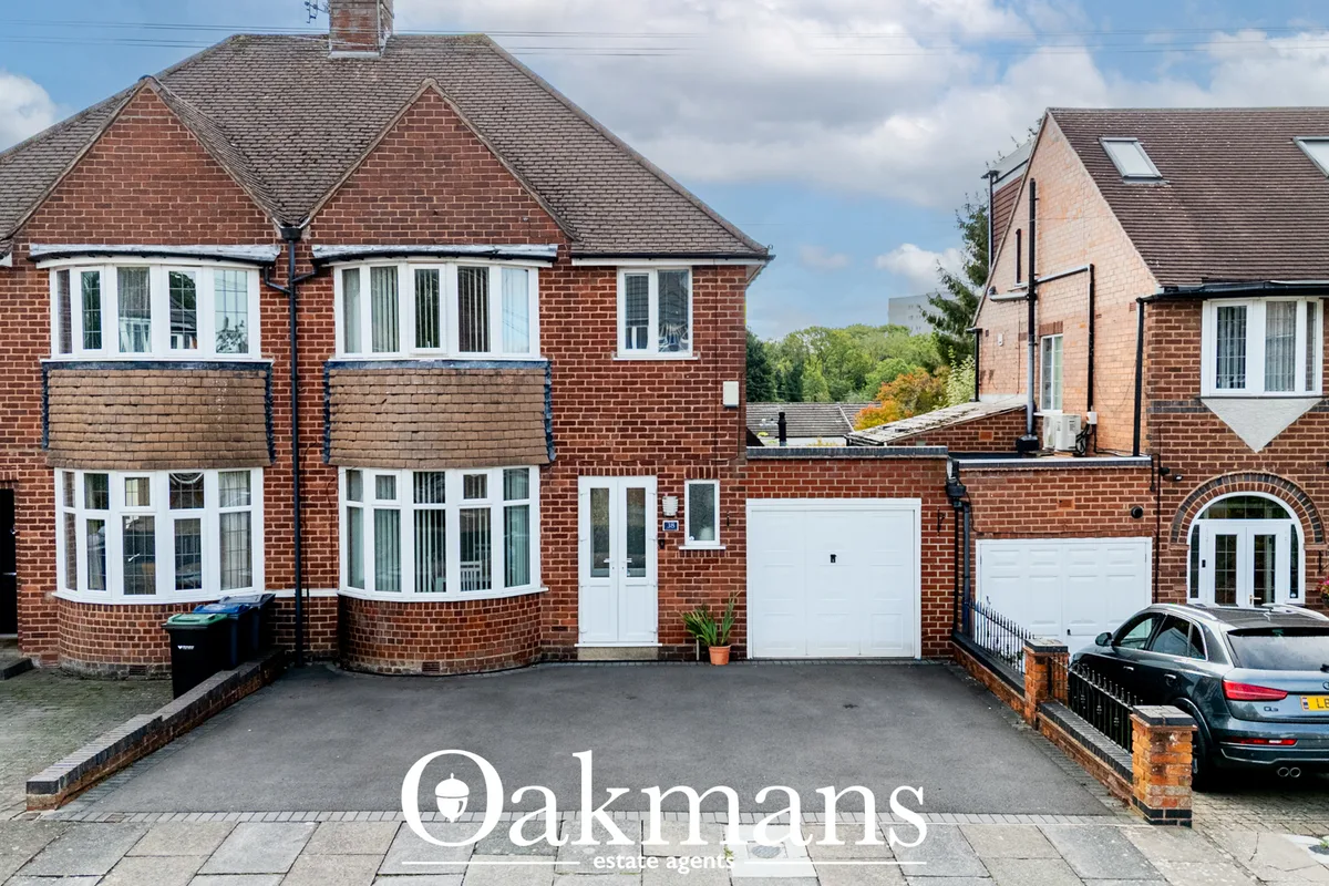 Red brick semi-detached house with bay windows, white garage door, driveway and parked Audi, neighbouring properties vis