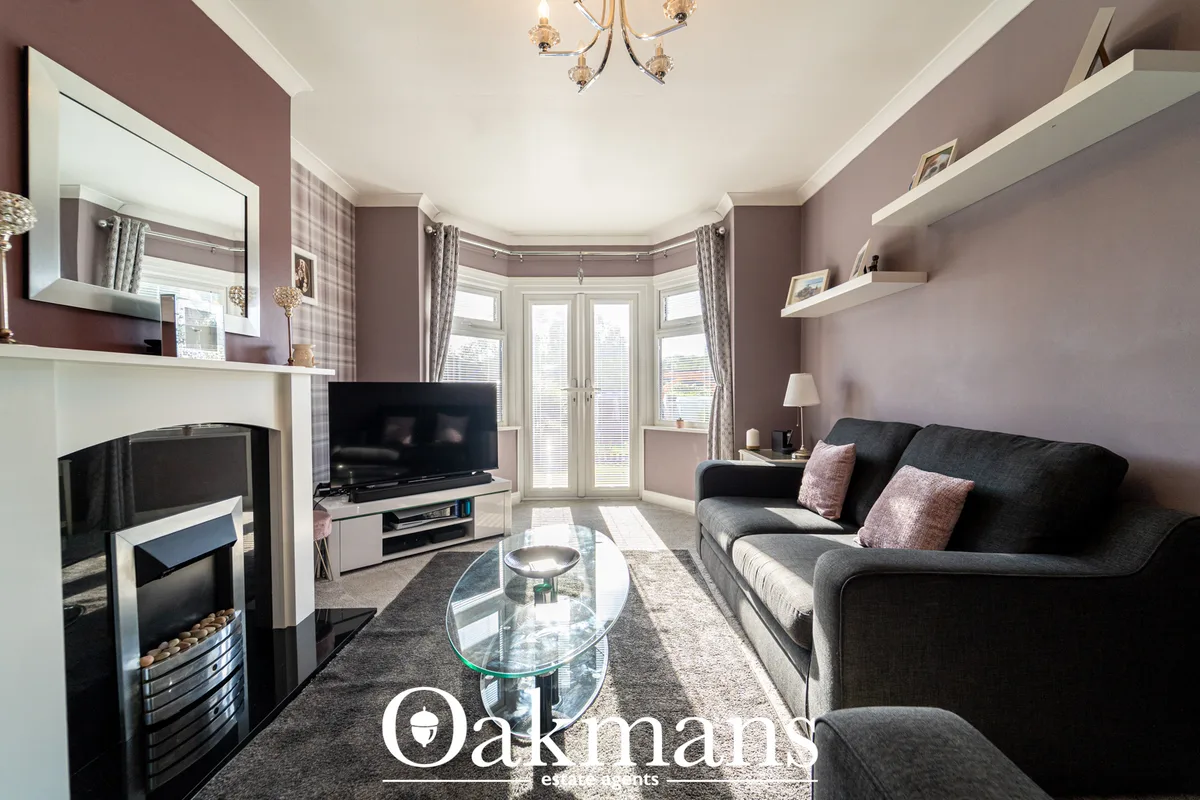 Contemporary living room with mauve walls, black sofa, fireplace, TV unit, bay windows with shutters and modern chandeli