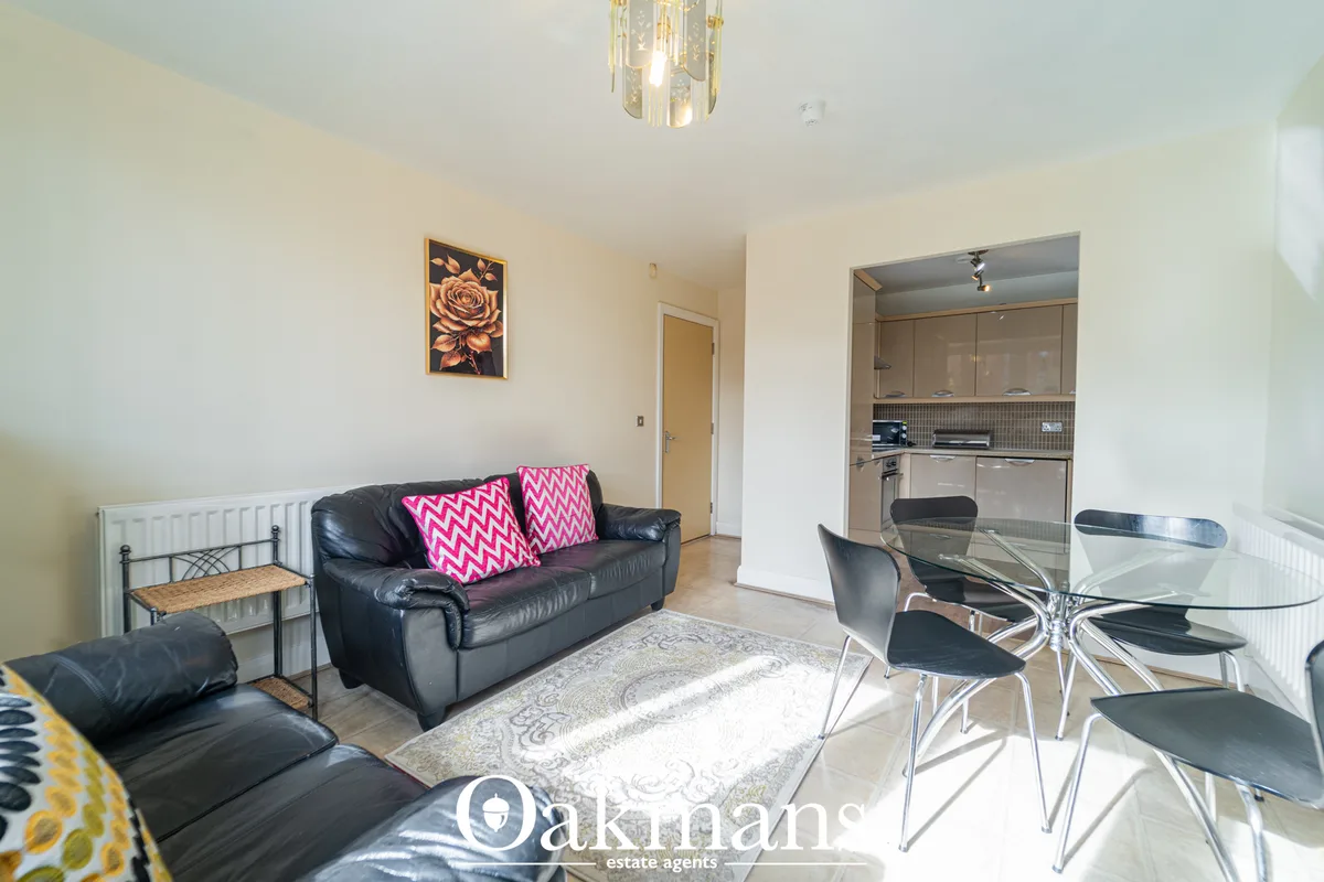 Open-plan living and dining area with black leather sofa, pink scatter cushions, glass dining table with chrome chairs, 