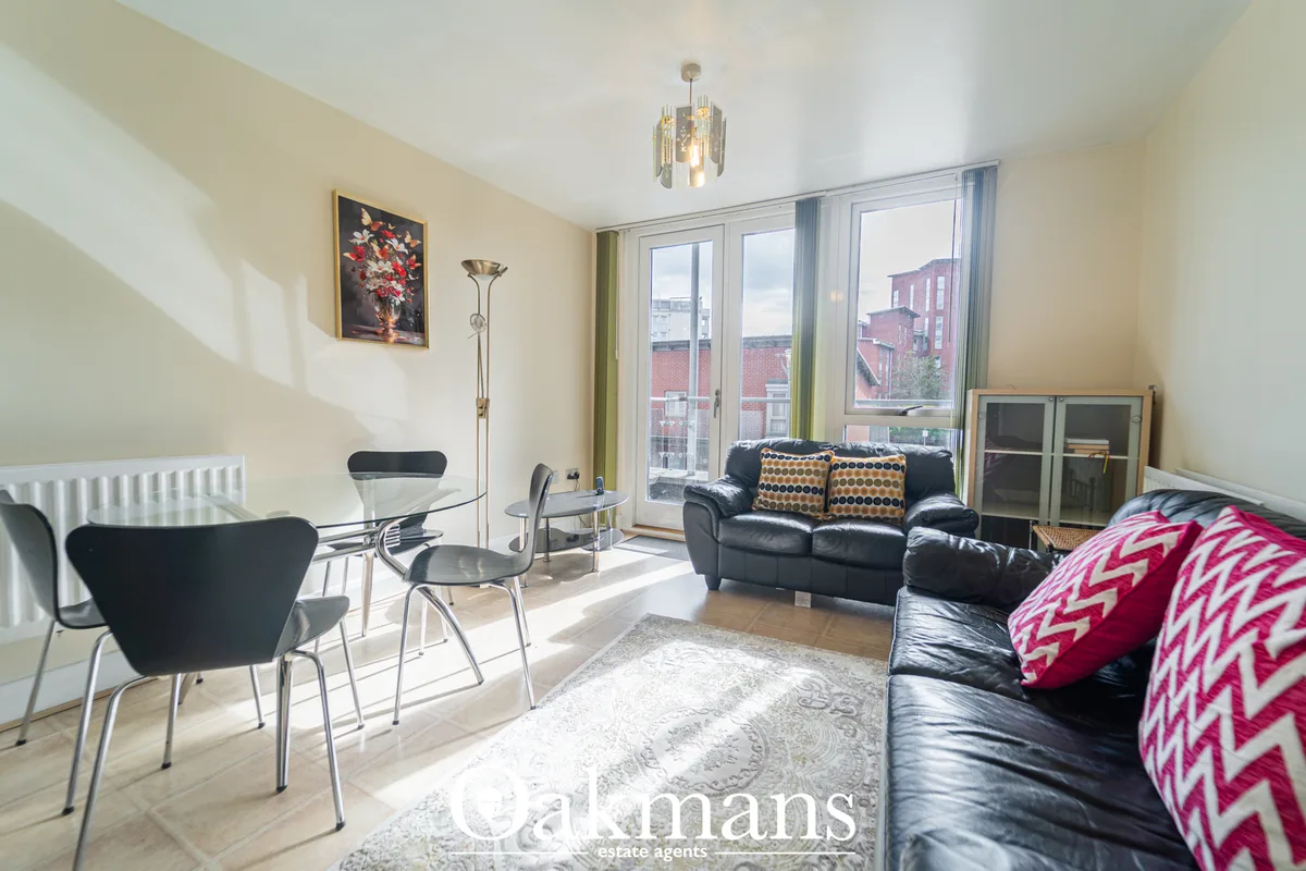 Bright open-plan living room with black leather sofa, dining chairs, floor-to-ceiling windows overlooking city, wooden f