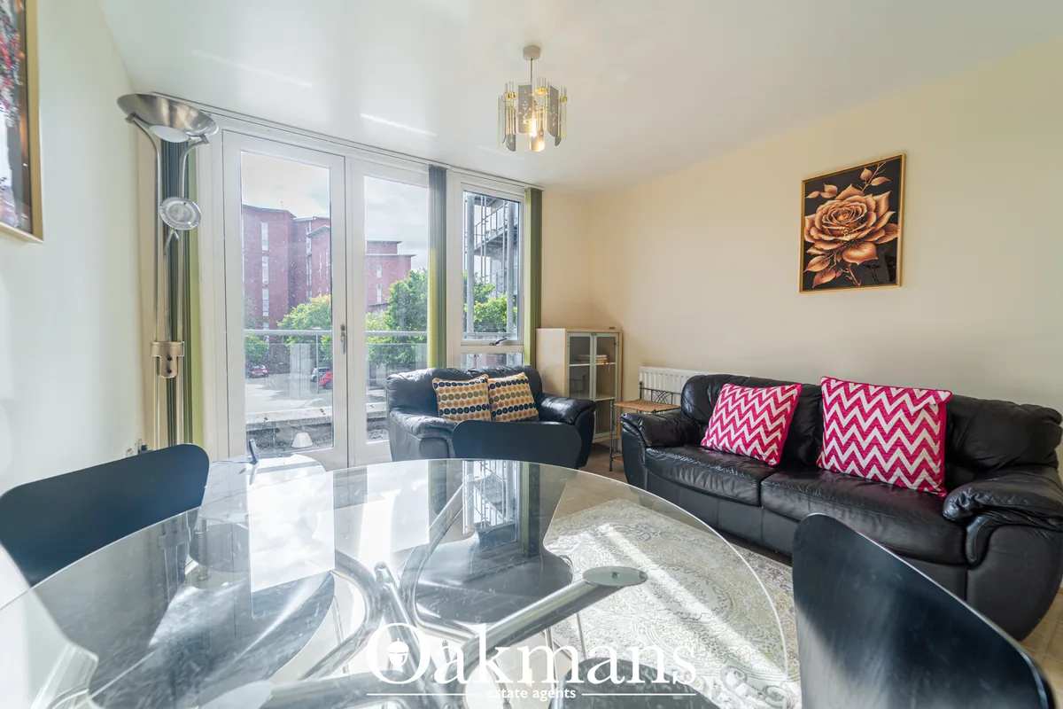 Bright living room with black leather sofas, glass coffee table, large windows overlooking urban street, pendant ceiling
