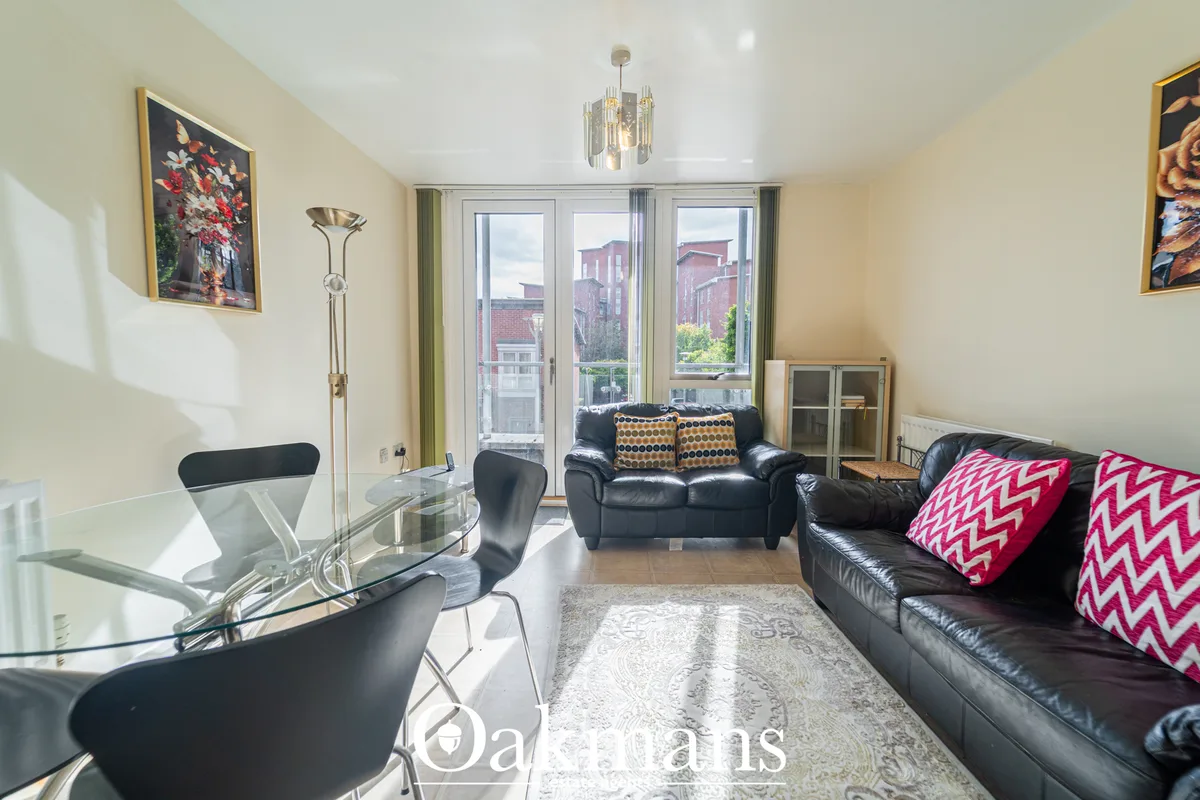 Bright living room with black leather sofas, glass desk, framed artwork, floor lamp, and triple-glazed windows overlooki