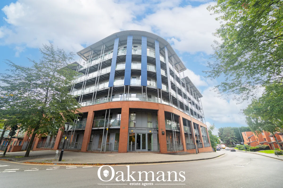 Modern curved apartment building with red brick base, white upper storeys and blue vertical supports, tree-lined street 