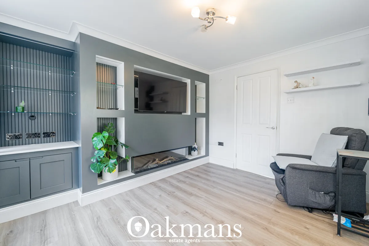 Modern living room with grey feature wall, built-in electric fireplace, wall-mounted TV, grey armchairs, wooden flooring