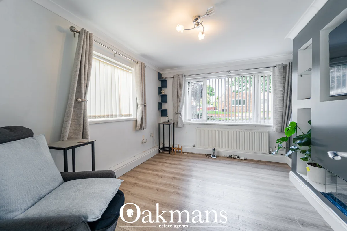 Bright living room with grey upholstered sofa, wooden flooring, large windows with vertical blinds and neutral décor