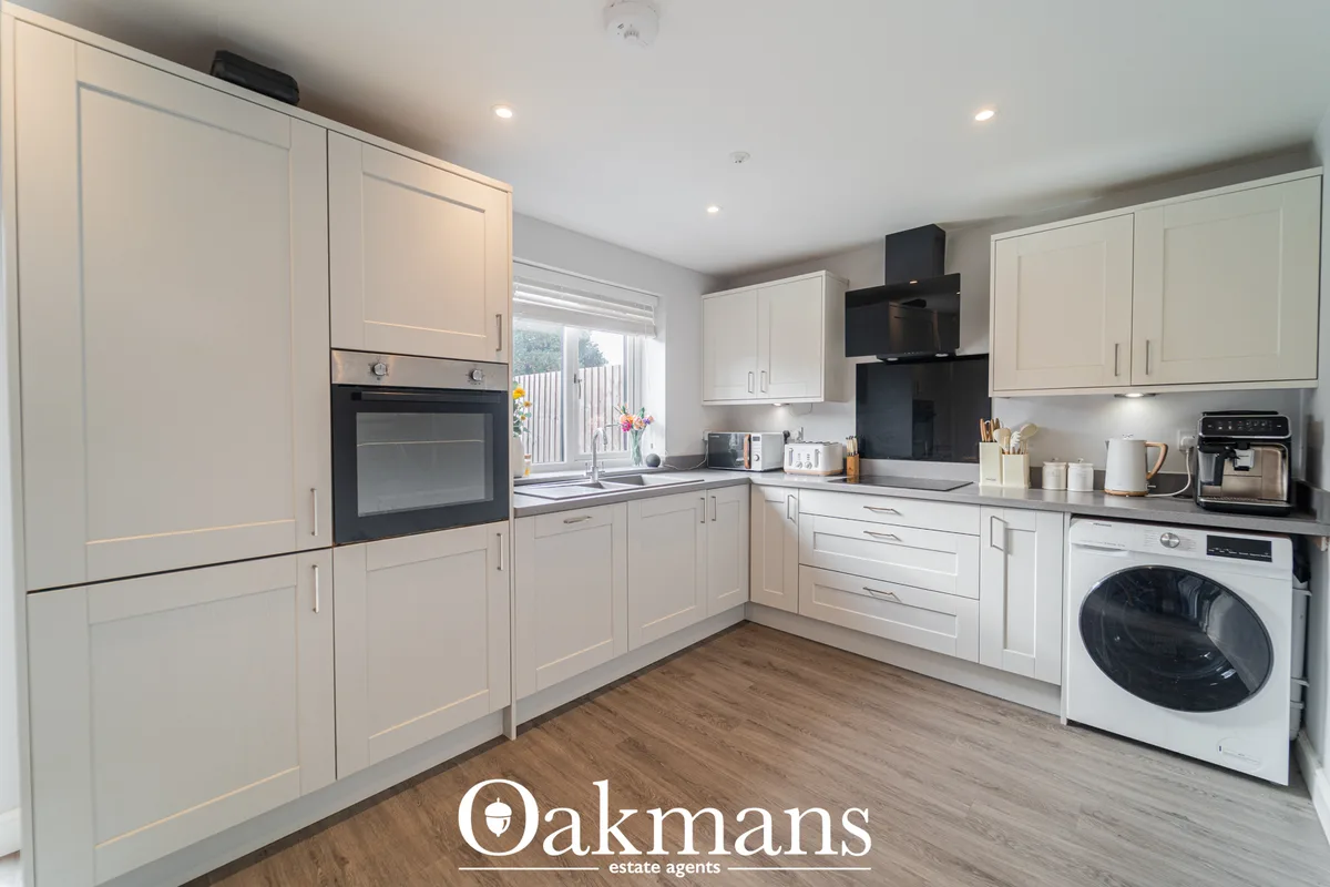 Modern fitted kitchen with cream cabinets, black oven and extractor, white worktops, washing machine, and wood-effect fl