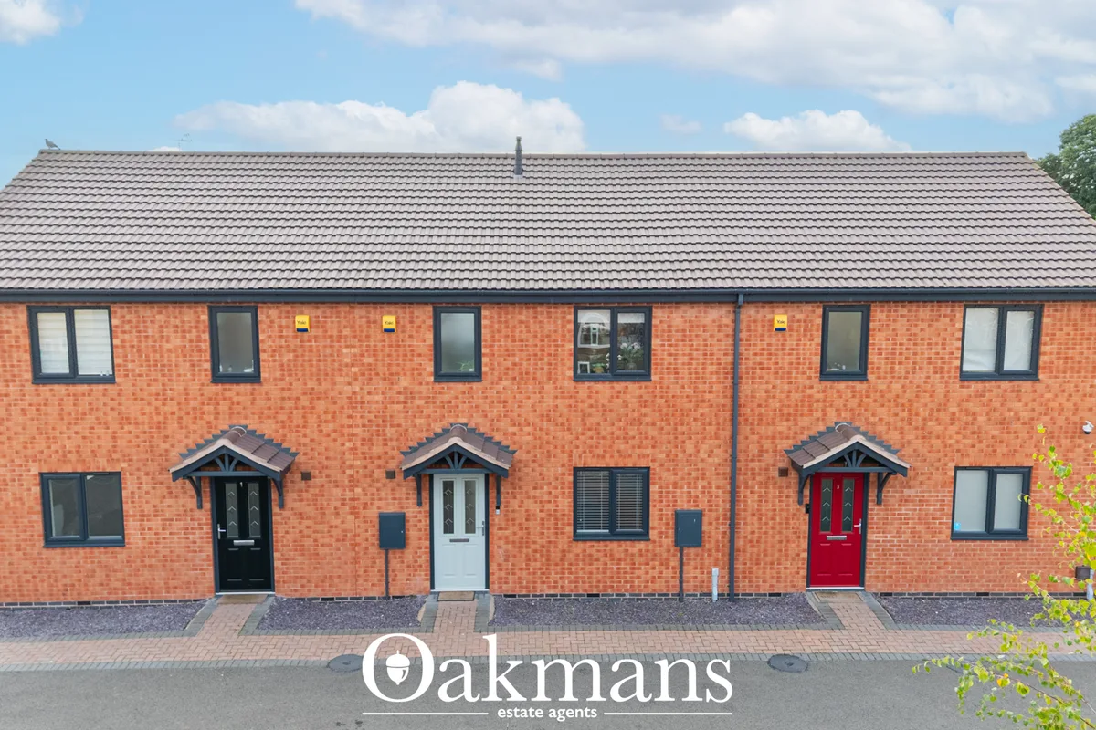 Red brick semi-detached residential building with three front doors, dark roof, windows, and brick paved forecourt