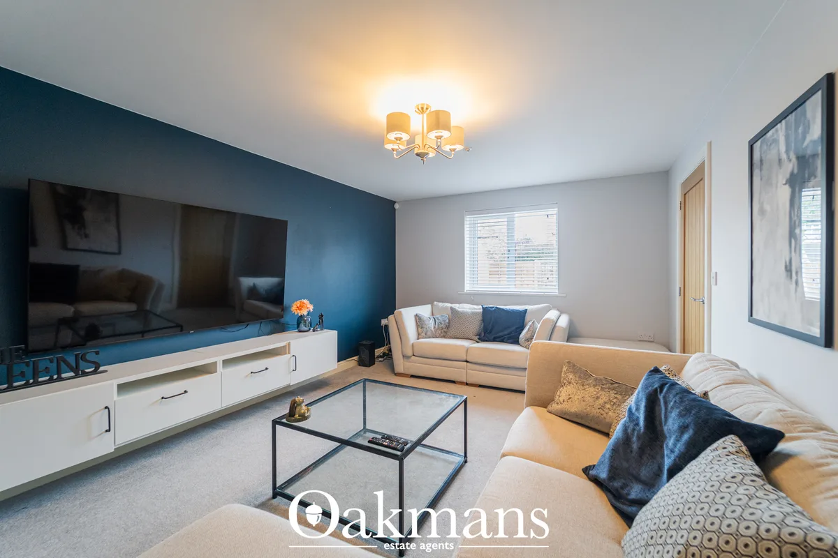 Contemporary living room with deep blue accent wall, cream corner sofa, large flat-screen TV, glass coffee table and cei