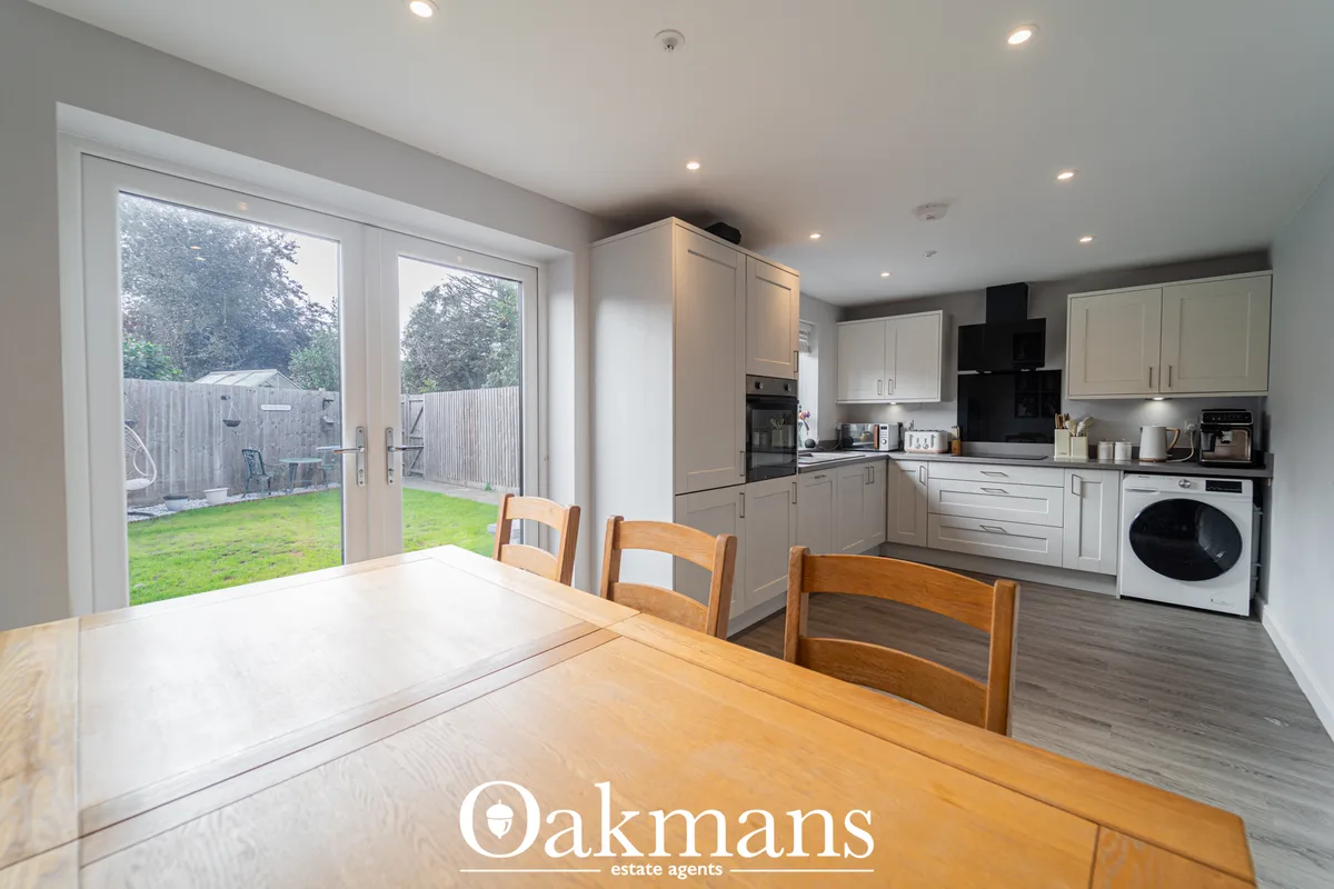 Open-plan kitchen and dining area with wooden dining table, white fitted units, black range cooker, washing machine, and