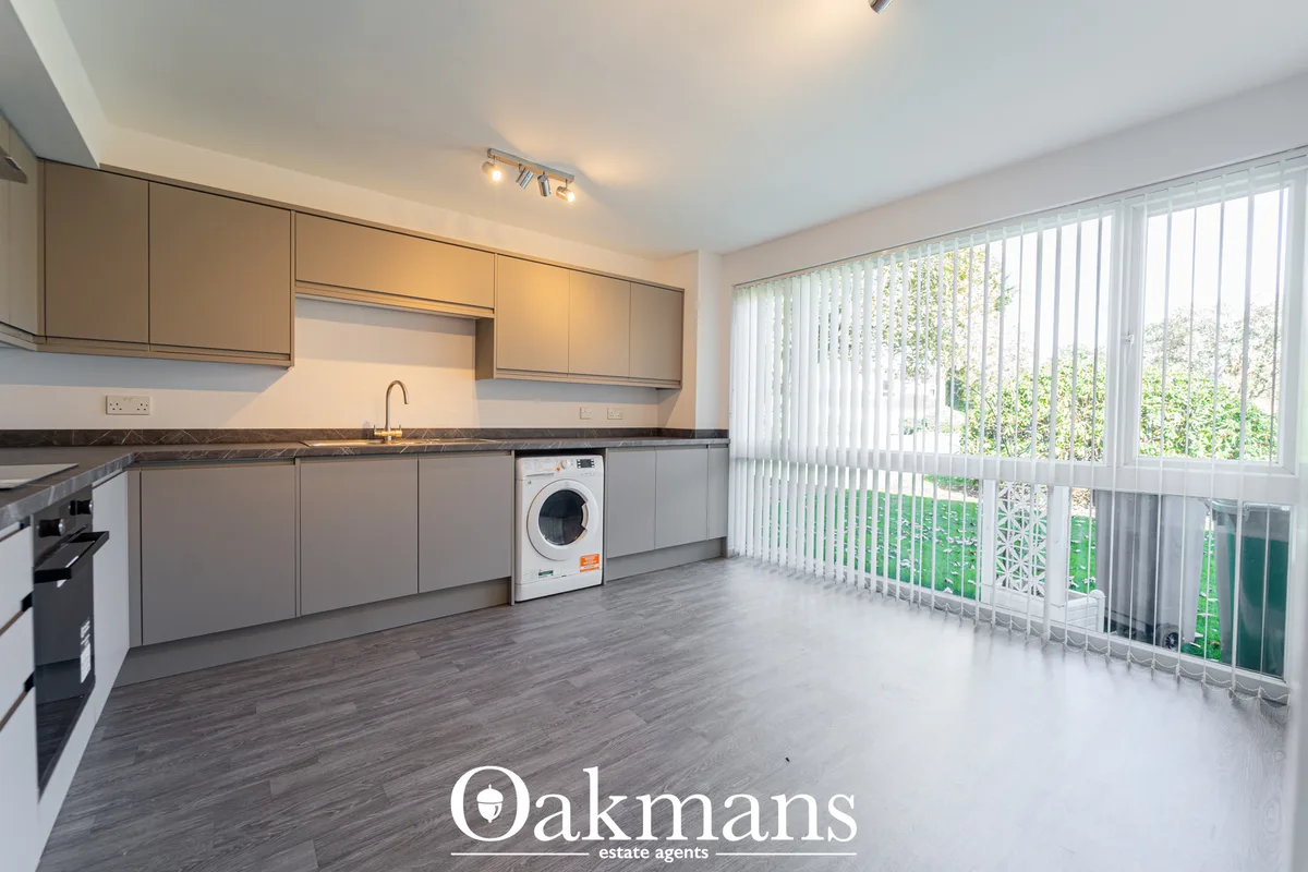 Modern kitchen with grey fitted units, dark worktops, integrated appliances, washing machine, and large windows overlook