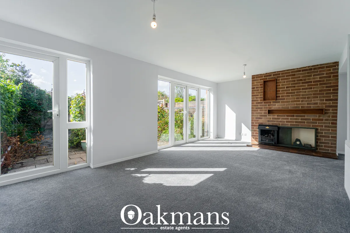 Spacious living room with grey carpet, white walls, brick fireplace with insert, multiple windows and glass doors openin