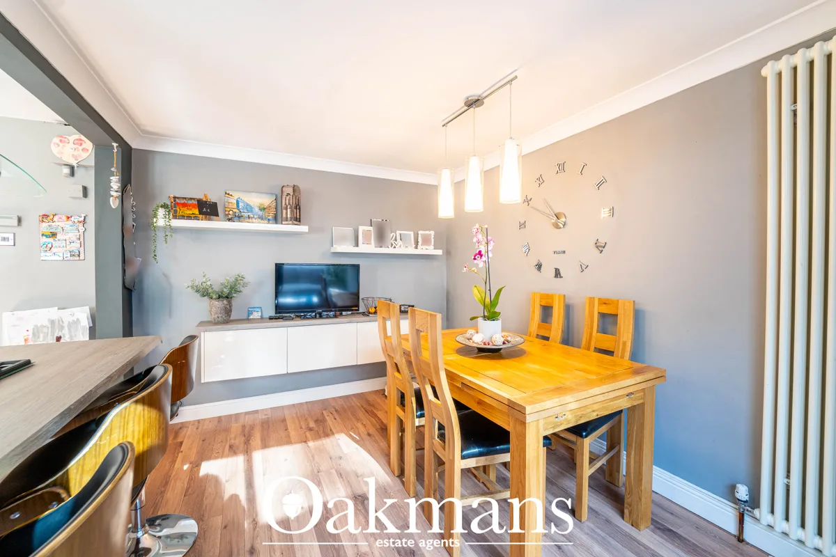 Bright dining room with wooden table, yellow chairs, open-plan kitchen and living area with TV, grey walls and pendant l