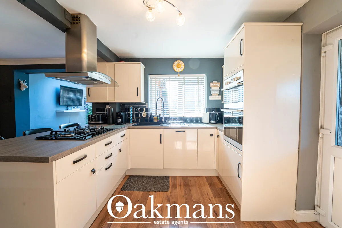 Modern fitted kitchen with cream units, dark worktops, blue feature wall, gas hob, built-in oven and wooden flooring